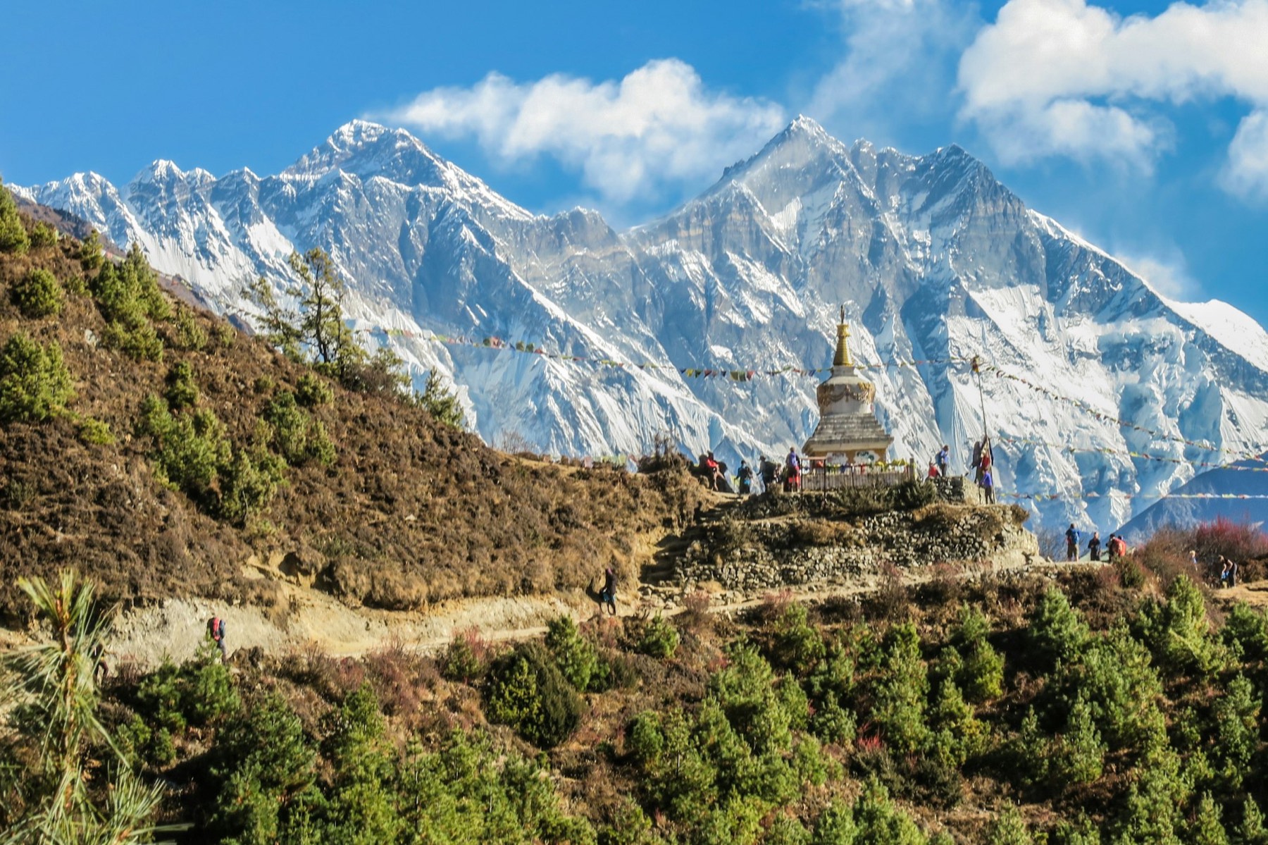 A stone stupa and prayer flags on a ridge, with snow-covered Himalayan peaks beyond